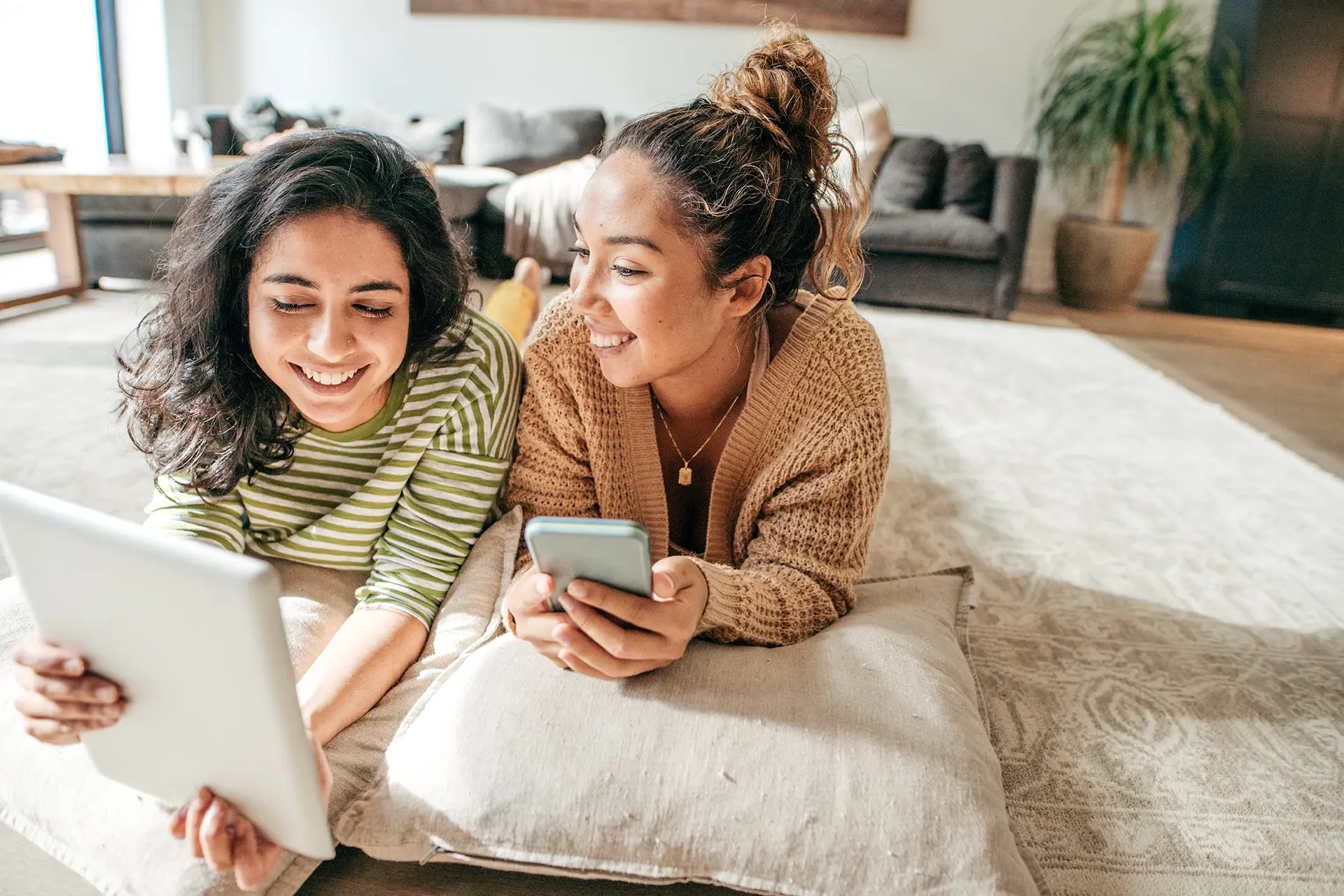 Two women relaxing on pillows looking at a tablet.