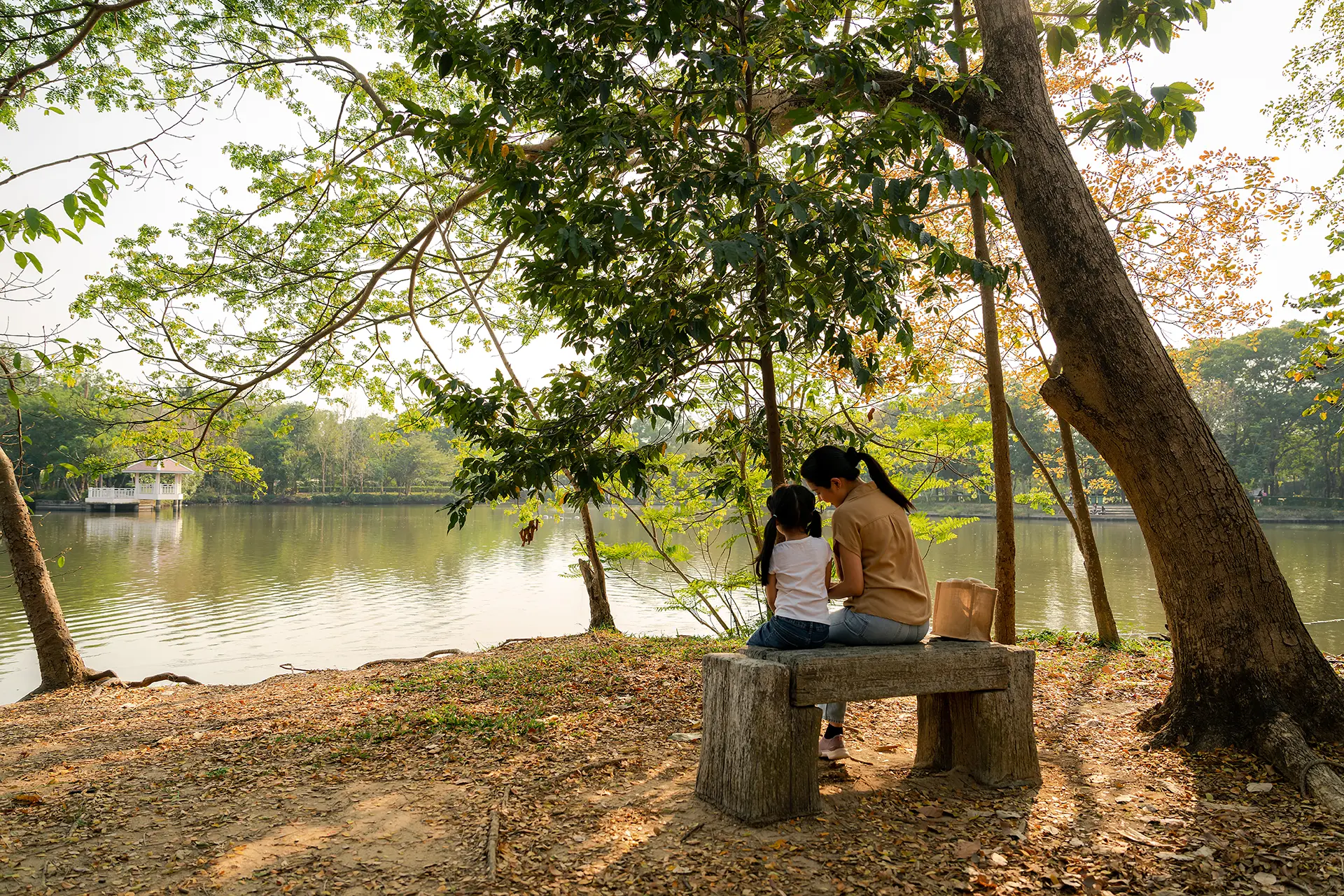 Woman and her daughter sitting on a bench by a pond